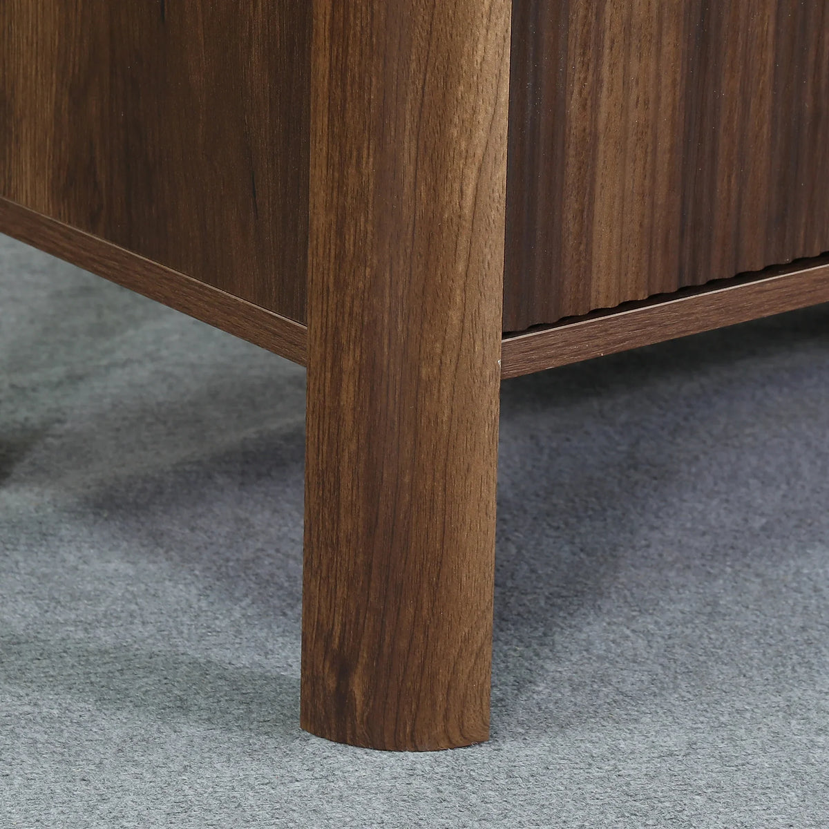 Close-up of a walnut wood furniture leg on a grey carpeted floor