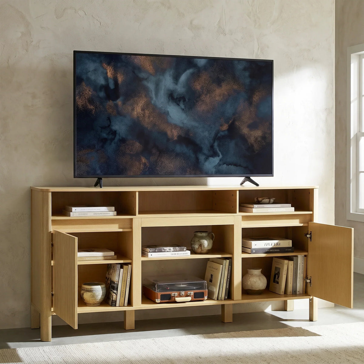 Modern light wood TV stand with open shelving and doors, holding a large flat screen TV.